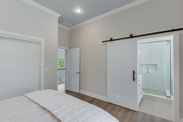 bedroom with a closet, wood-type flooring, crown molding, ensuite bath, and a barn door