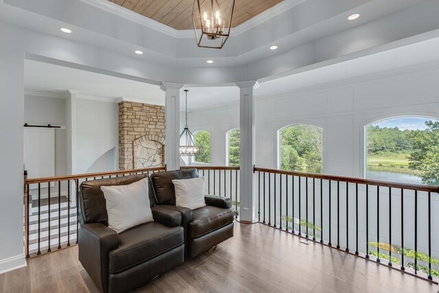 sitting room featuring wood-type flooring, a raised ceiling, a notable chandelier, and ornamental molding