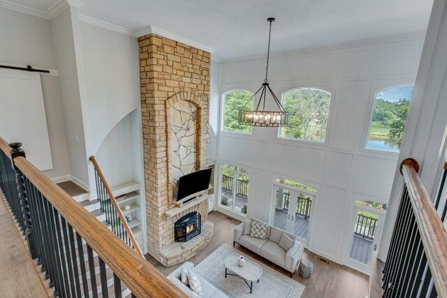 living room featuring an inviting chandelier, a wood stove, hardwood / wood-style floors, ornamental molding, and a brick fireplace