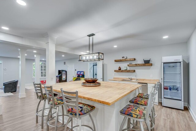 kitchen featuring dishwasher, light hardwood / wood-style flooring, pendant lighting, butcher block counters, and a breakfast bar