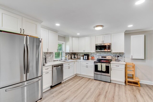 kitchen with white cabinets, backsplash, light wood-type flooring, appliances with stainless steel finishes, and sink