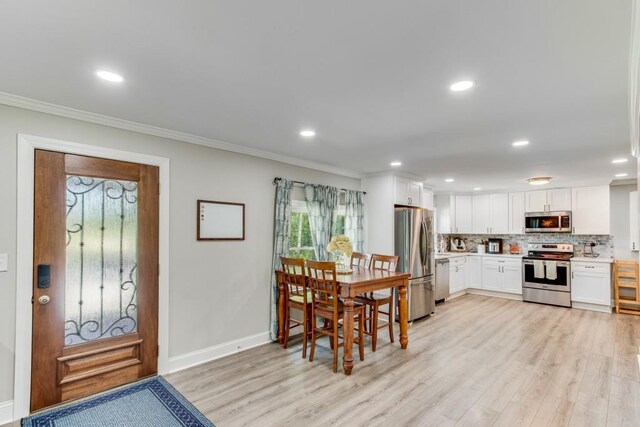 kitchen with light hardwood / wood-style flooring, backsplash, crown molding, stainless steel appliances, and white cabinetry