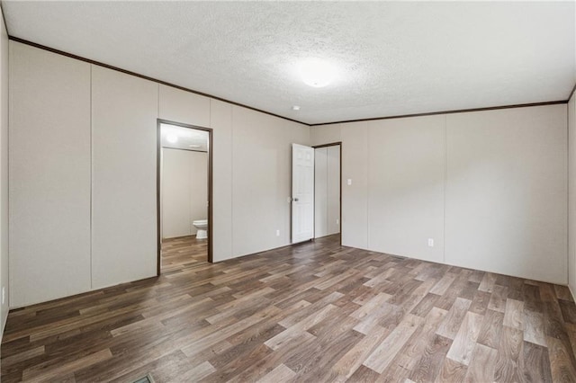 unfurnished bedroom featuring wood finished floors, a textured ceiling, ornamental molding, and connected bathroom