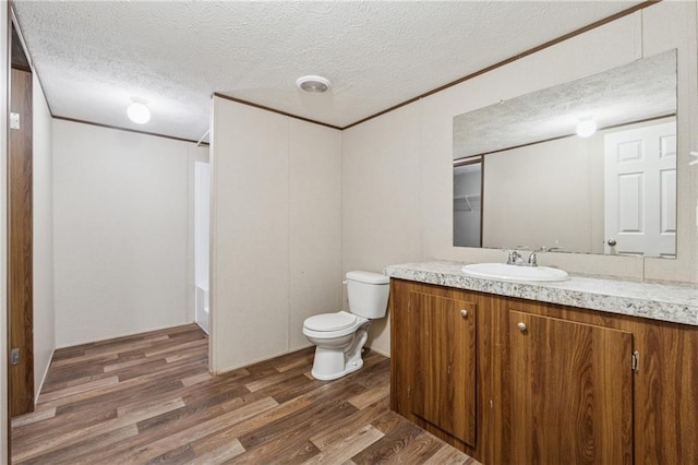 full bathroom featuring toilet, ornamental molding, wood finished floors, and a textured ceiling