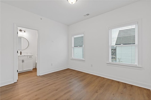 unfurnished bedroom featuring ensuite bath, multiple windows, and light hardwood / wood-style flooring