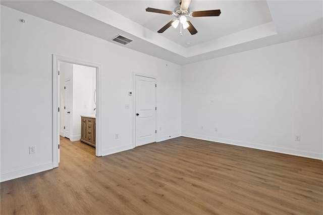 unfurnished bedroom with ceiling fan, ensuite bathroom, light hardwood / wood-style floors, and a tray ceiling