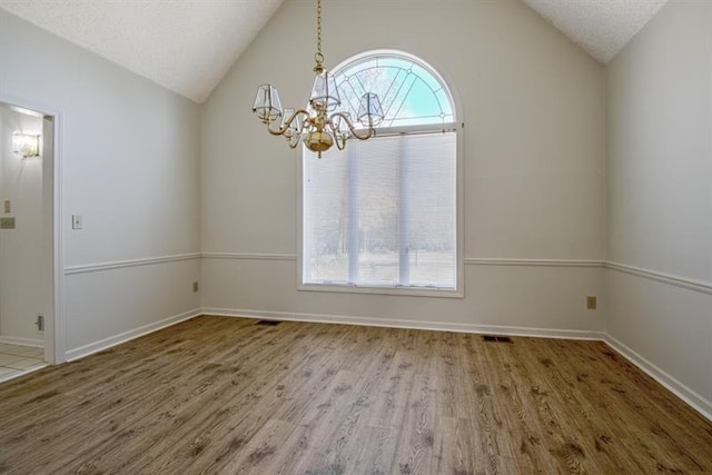 empty room with hardwood / wood-style flooring, lofted ceiling, a healthy amount of sunlight, and a chandelier