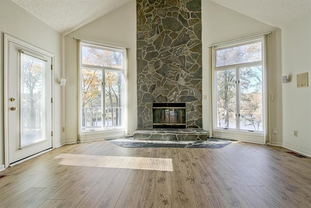 unfurnished living room with hardwood / wood-style floors, a stone fireplace, high vaulted ceiling, and a textured ceiling