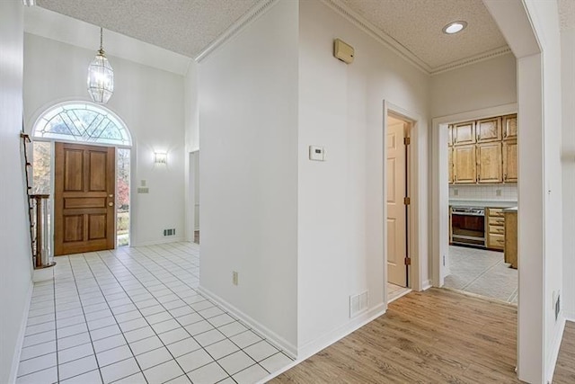 tiled entrance foyer featuring an inviting chandelier, ornamental molding, and a textured ceiling