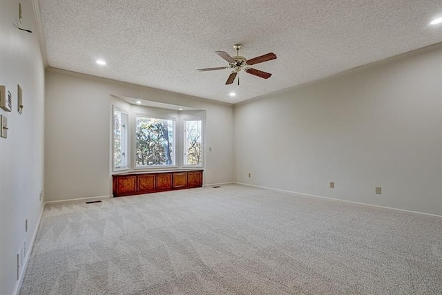 carpeted spare room featuring ceiling fan, ornamental molding, and a textured ceiling