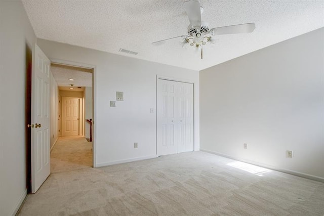 unfurnished bedroom with ceiling fan, light colored carpet, a closet, and a textured ceiling