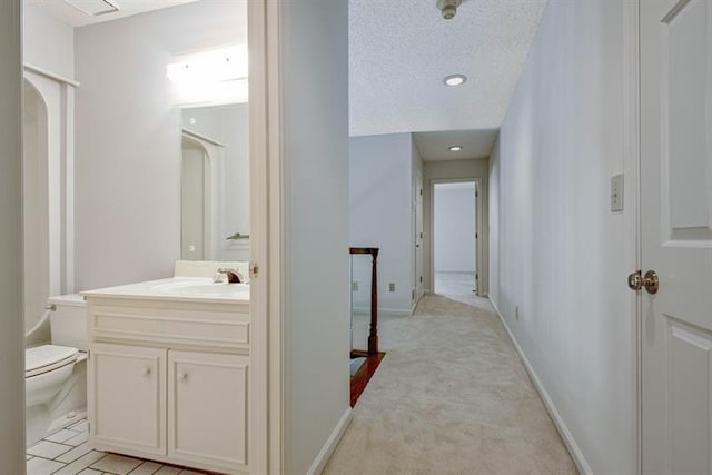 corridor with light colored carpet, sink, and a textured ceiling