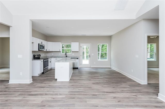 kitchen featuring baseboards, stainless steel appliances, white cabinetry, open floor plan, and a center island