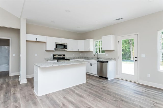 kitchen featuring visible vents, a center island, light wood-style flooring, white cabinets, and stainless steel appliances