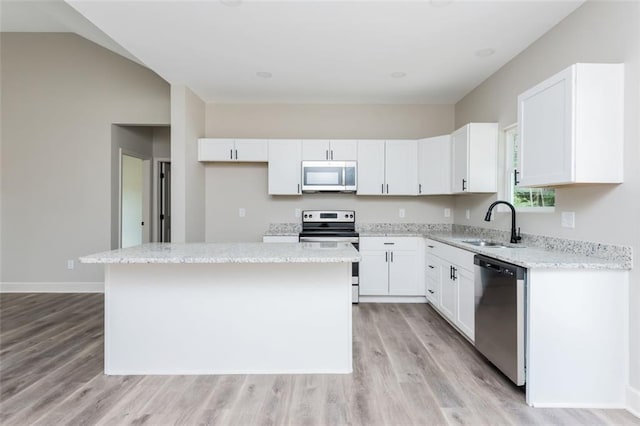 kitchen with a sink, light stone counters, a kitchen island, appliances with stainless steel finishes, and white cabinets