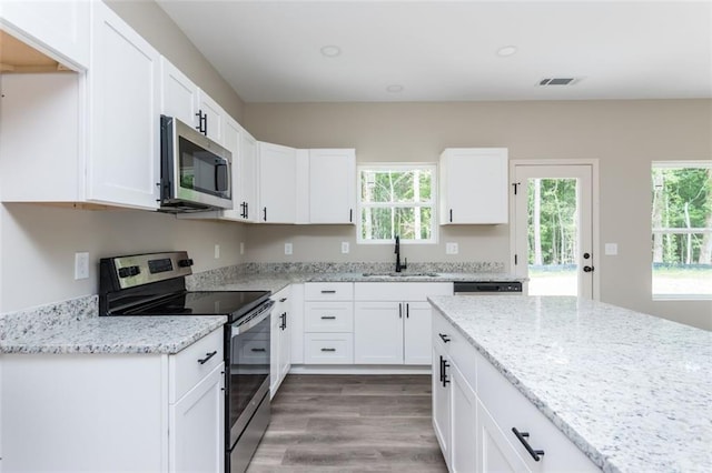 kitchen featuring visible vents, a sink, stainless steel appliances, white cabinets, and light stone countertops