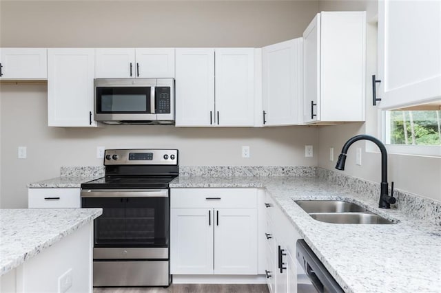 kitchen with white cabinets, light stone counters, appliances with stainless steel finishes, and a sink