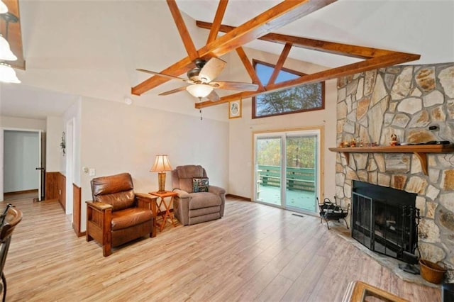 sitting room featuring ceiling fan, a stone fireplace, beamed ceiling, high vaulted ceiling, and light wood-type flooring