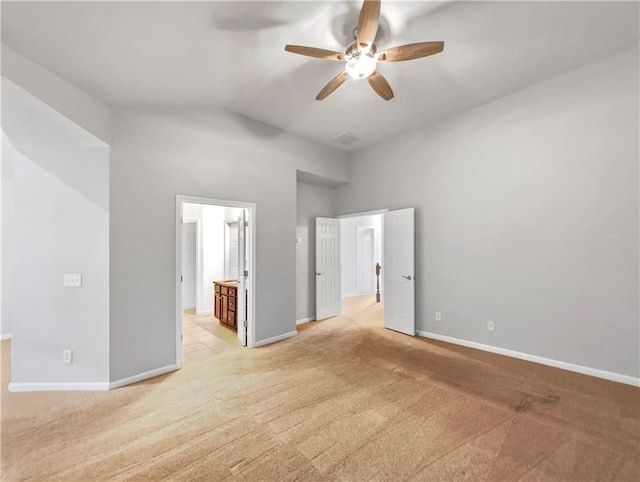 unfurnished bedroom featuring a high ceiling, ensuite bath, ceiling fan, and light colored carpet