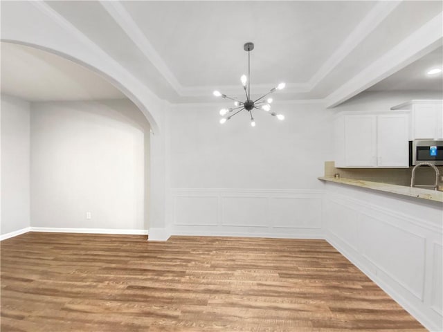 unfurnished dining area with sink, a notable chandelier, light wood-type flooring, and a tray ceiling