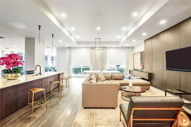 living room featuring sink, light wood-type flooring, and a tray ceiling