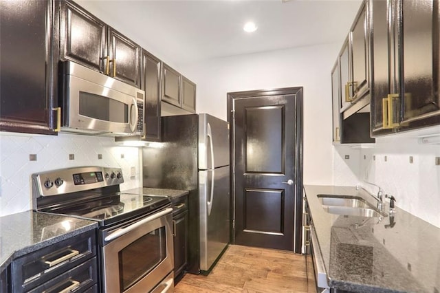 kitchen featuring appliances with stainless steel finishes, sink, backsplash, dark stone counters, and light wood-type flooring