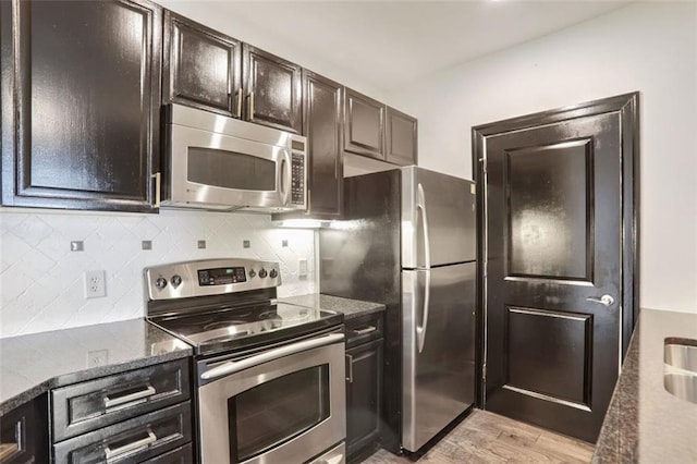 kitchen with light hardwood / wood-style flooring, appliances with stainless steel finishes, backsplash, dark brown cabinetry, and dark stone counters