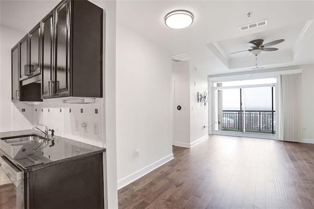 kitchen featuring sink, dark wood-type flooring, dishwasher, a raised ceiling, and dark stone counters