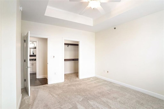 unfurnished bedroom with ceiling fan, light colored carpet, a tray ceiling, and a closet