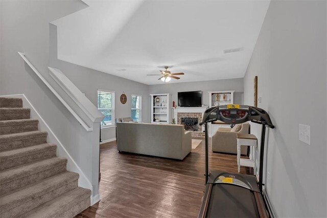 living room featuring ceiling fan, a fireplace, and dark wood-type flooring