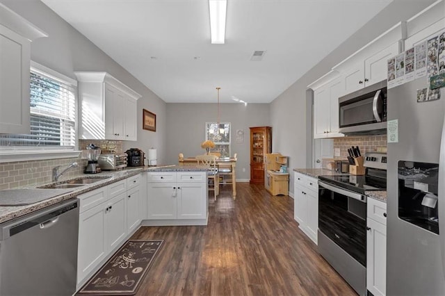 kitchen with backsplash, stainless steel appliances, sink, decorative light fixtures, and white cabinetry