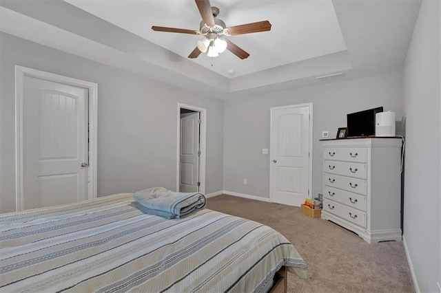 carpeted bedroom featuring a tray ceiling and ceiling fan