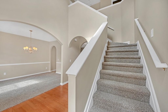 stairway with a high ceiling, hardwood / wood-style floors, and an inviting chandelier