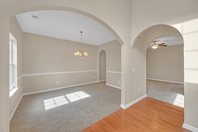 empty room with ceiling fan with notable chandelier and wood-type flooring