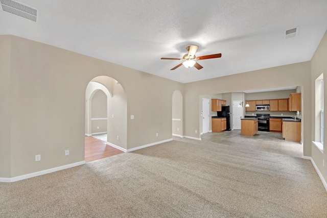 unfurnished living room with light carpet, a textured ceiling, and ceiling fan