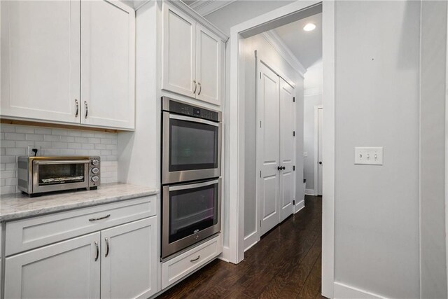 kitchen featuring double oven, dark wood-type flooring, light stone counters, white cabinets, and ornamental molding