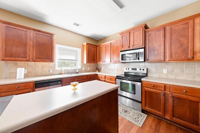 kitchen with sink, backsplash, light hardwood / wood-style flooring, and appliances with stainless steel finishes