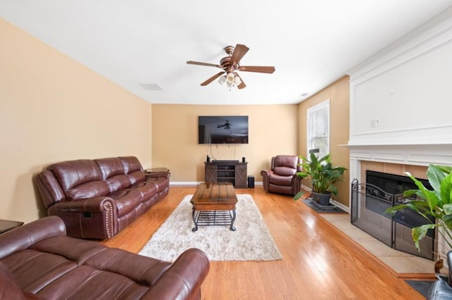 living room featuring ceiling fan, light hardwood / wood-style flooring, and a tiled fireplace