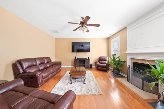 living room with a tile fireplace, baseboards, ceiling fan, and light wood finished floors