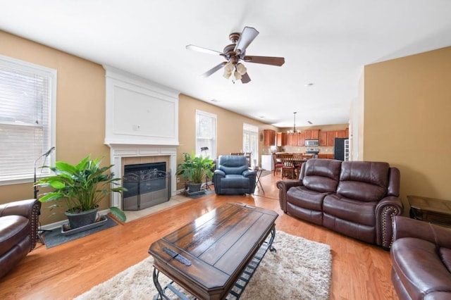living room featuring ceiling fan, light wood finished floors, and a tile fireplace