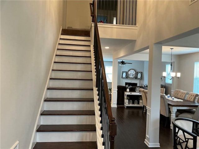 staircase with a fireplace, visible vents, a towering ceiling, wood finished floors, and ceiling fan with notable chandelier