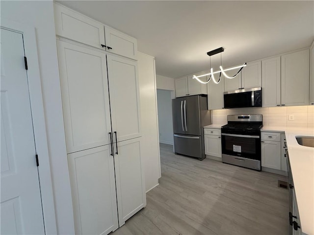 kitchen with decorative light fixtures, decorative backsplash, white cabinets, and appliances with stainless steel finishes