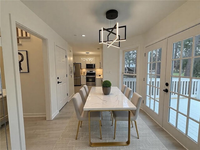 dining area featuring a notable chandelier, light hardwood / wood-style flooring, french doors, and a healthy amount of sunlight