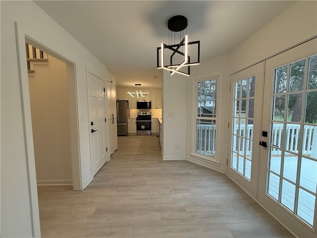 interior space featuring french doors, a healthy amount of sunlight, a notable chandelier, and light hardwood / wood-style flooring