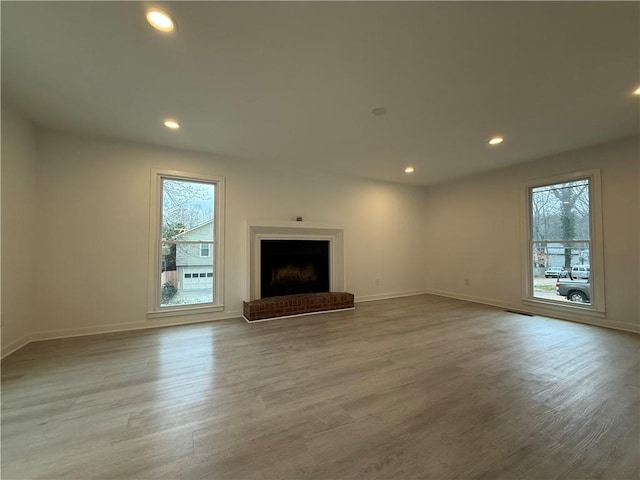 unfurnished living room featuring a healthy amount of sunlight, a brick fireplace, and light hardwood / wood-style flooring