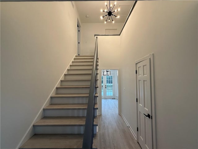 stairs with a high ceiling, wood-type flooring, and a chandelier