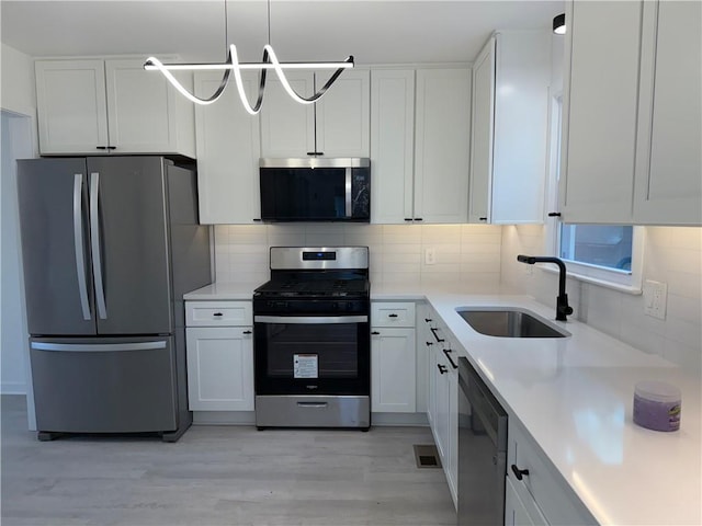 kitchen with pendant lighting, sink, stainless steel appliances, white cabinets, and decorative backsplash