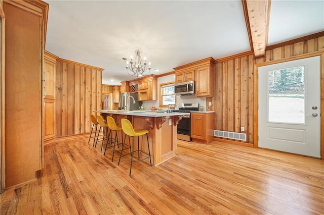 kitchen with a kitchen island with sink, beamed ceiling, light hardwood / wood-style floors, and appliances with stainless steel finishes