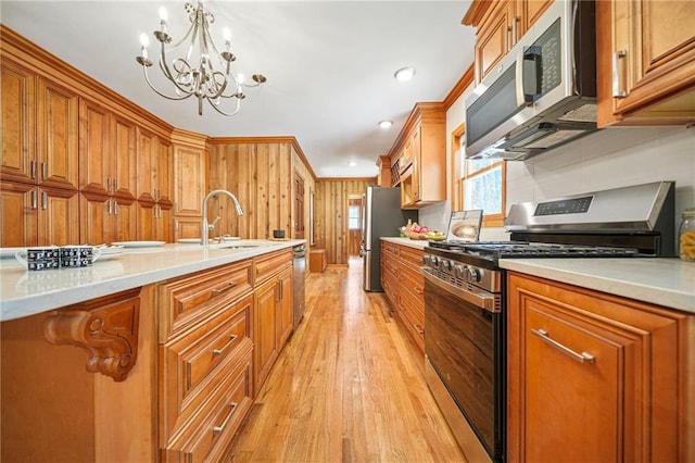 kitchen featuring sink, hanging light fixtures, stainless steel appliances, a notable chandelier, and light wood-type flooring