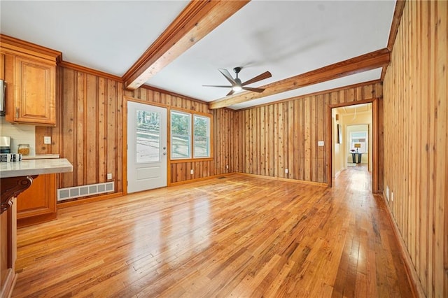 unfurnished living room with beam ceiling, light hardwood / wood-style floors, ceiling fan, and wood walls